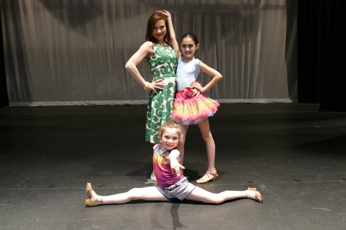 Three performers on a dark stage, one in the splits